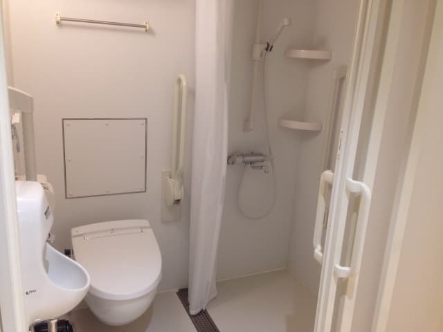 介護向けのトイレ併設シャワールーム、手すりとカーテンを備えたバリアフリー設計の事例写真
