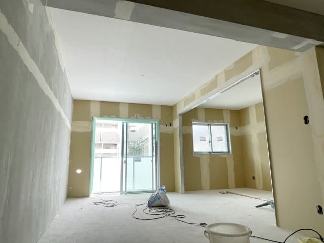 20畳の広いリビング等のクロス張り替え工事において、工期に影響する重要な工程である壁面の下地パテ処理（平滑化）が行われた施工現場の様子