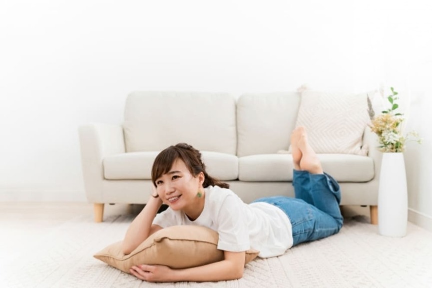 床暖房リフォームを実施したリビングで快適そうに寝そべって微笑む女性