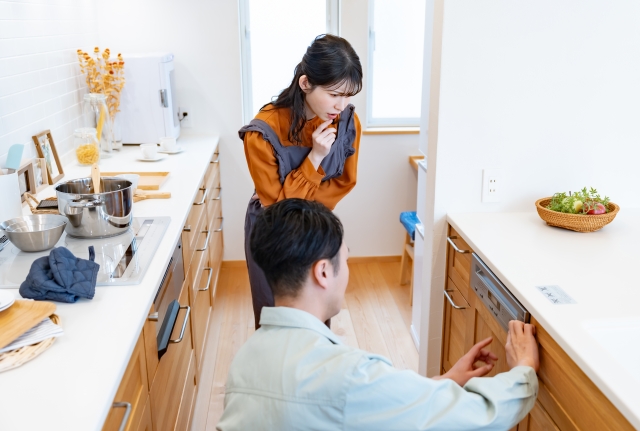 夫婦がキッチンのキャビネットに設置されたビルトイン食洗機の状態を確認・検討している様子。