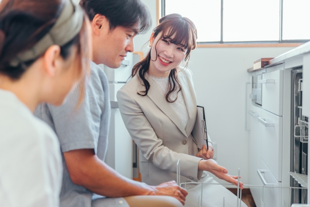 リフォーム会社のスタッフが夫婦にビルトイン食洗機の設置について説明している様子。