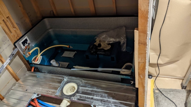 マンションリフォーム工事中の浴室施工場面。ユニットバスの浴槽を上から見た状態で、給水管・排水管の配管接続が露出している。築古マンションの水回りリフォームにおける浴室交換工事の事例。