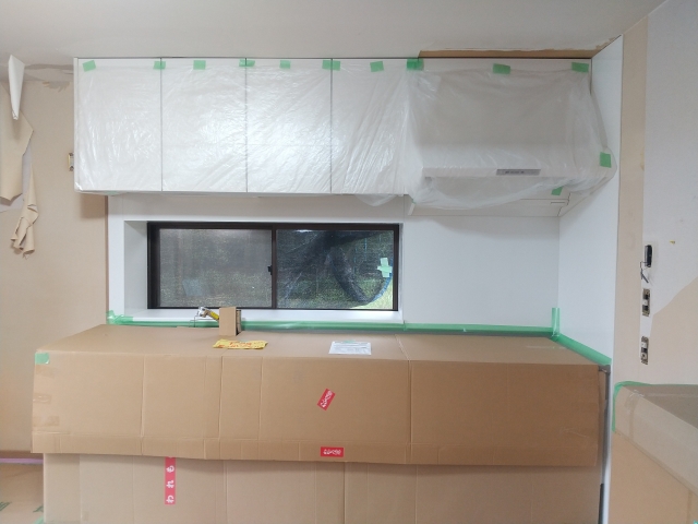 マンションリフォーム工事中のキッチン施工場面。吊り戸棚と天板をビニールと段ボールで養生した状態。築古マンションの水回りリフォームにおけるキッチン交換工事の事例。