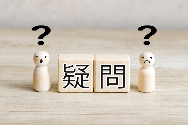 「疑問」と書かれた木製ブロックとクエスチョンマークが付いた木製人形。トイレへのエコカラット導入に関するよくある質問を表すイメージ画像。