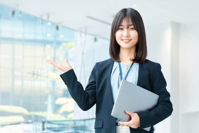 ノートパソコンを抱えて笑顔で案内する女性スタッフ。トイレのエコカラット施工や業者選びのご相談受付を表すイメージ画像。