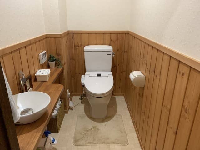 木目調の腰壁と木製カウンターに丸型ボウルを設置したトイレ手洗い器。費用が高額になりやすいカウンタータイプや内装工事を伴う施工例