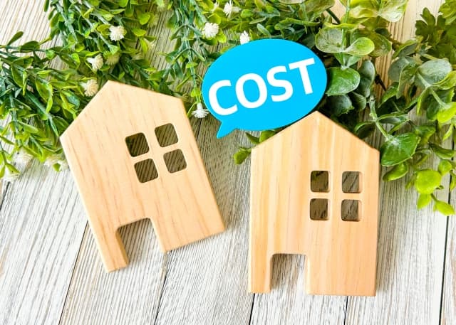 「COST」と書かれた吹き出しと家のオブジェ。トイレの手洗い器後付けにおける給排水工事費用やリフォーム費用目安のイメージ画像